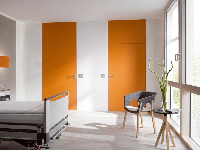 White hospital room with two orange doors fitted with a lever handle in the color grey made of polyamide