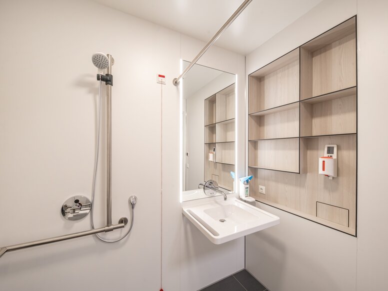 Salle de bain du patient avec lavabo et espace douche équipé d'un lavabo et d'un support de douche en acier inoxydable